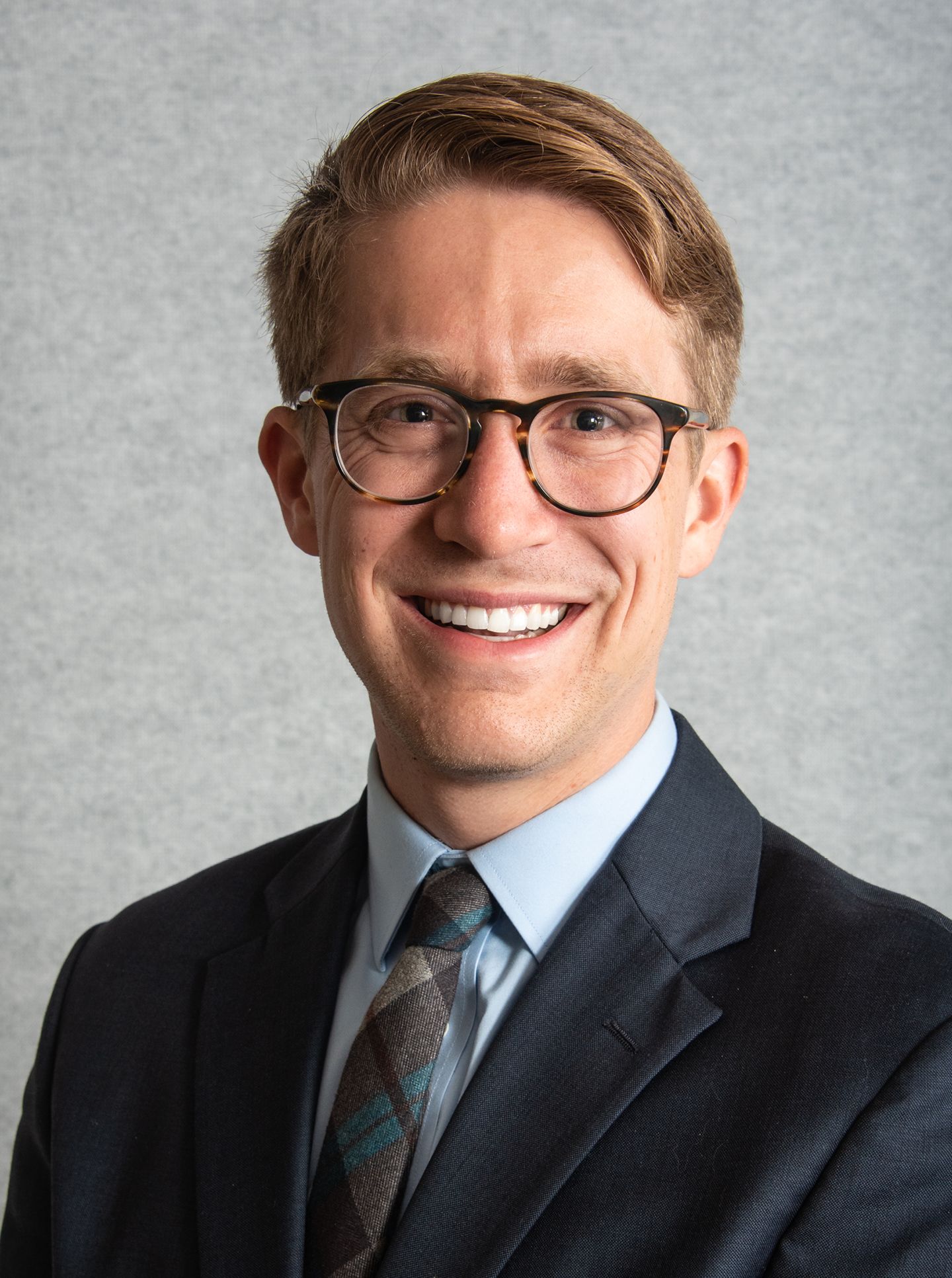 Head shot of man in suit and tie with glasses and red hair smiling.